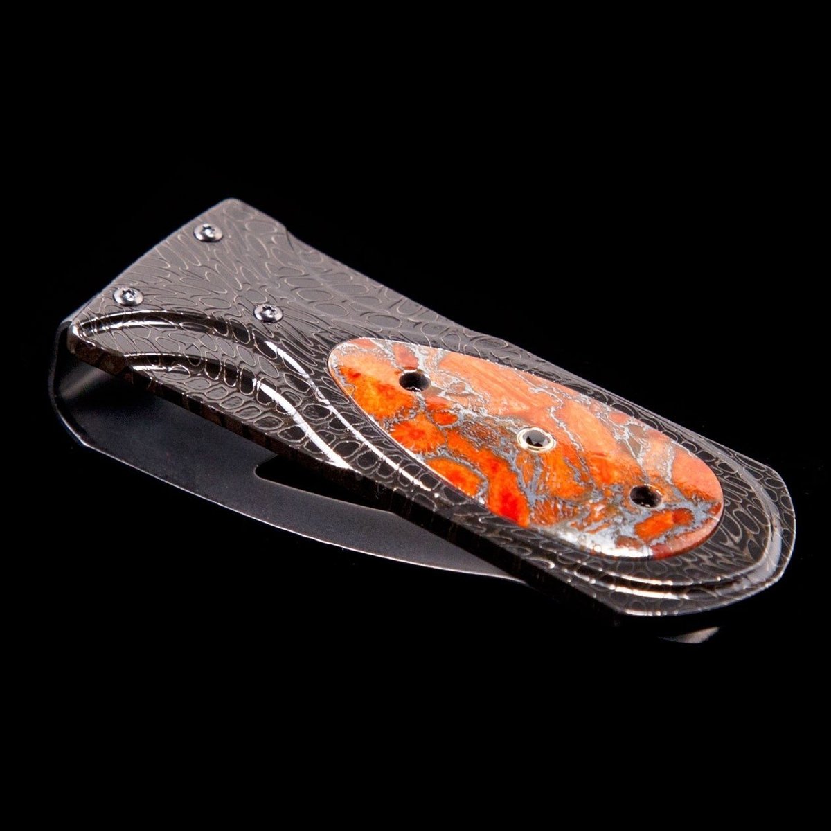 William Henry Money Clip
Frame/Body: Hand-Forgrd 'River Rock' Damascus 
Scale/Inlay: 'Zinc Matrix'apple Coral
Clip: Tempered Stainless Steel, With A Beautiful Engraving Bright Cut Against The Matte-Finished Background.
Gemstones/Embellishments: Spinel